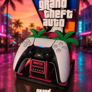 Könnte beinhalten: Ein schwarz-weißer Controller-Ständer mit einem großen Grand Theft Auto V-Logo, zwei grünen Palmen und einem kleinen rechteckigen Schild mit der Aufschrift WANTED GAMERTAG und fünf gelben Sternen. Ein separater Grand Theft Auto VI-Schlüsselanhänger liegt bei.