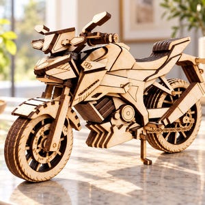 Könnte beinhalten: Ein detailliertes Holzmodell eines Motorrads, gefertigt aus hellen Sperrholzteilen. Das Modell zeigt ein Vorderrad mit sichtbaren Bremsscheiben, einen Kraftstofftank, einen Sitz, ein Hinterrad mit Kettenantrieb und einen Seitenständer.