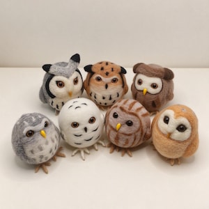 May include: A collection of seven needle-felted owl figurines in various colors including white, gray, brown, and tan. Each owl features round dark eyes, a small yellow beak, and textured wool bodies with distinct patterns and small feet.
