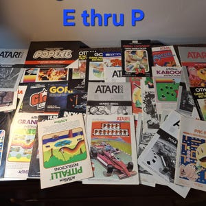 May include: A collection of vintage Atari 2600 video game instruction manuals featuring colorful cover art for titles including Pac-Man, Pitfall, Pole Position, Mario Bros, and Missile Command, with the blue text E thru P displayed at the top.