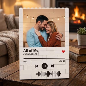 Op de afbeelding: Een rechthoekig wit frame in baksteenstijl met een foto van een knuffelend stel. Het frame toont de tekst "All of Me" en "John Legend" met een rood hartpictogram, een voortgangsbalk, de tijden 0:01 en -04:40 en een geluidsgolfgrafiek.