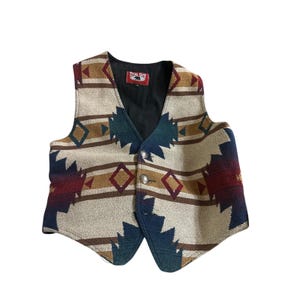 May include: A sleeveless vest featuring a woven geometric pattern in cream, navy blue, dark red, and tan. The vest has a black interior lining, a True Grit brand label at the neckline, and two silver-toned metal buttons on the front closure.
