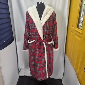 May include: A long-sleeved robe featuring a red, green, and white plaid pattern. The garment includes a white sherpa-lined hood, matching white sherpa trim along the front opening and cuffs, and a matching fabric tie belt at the waist.