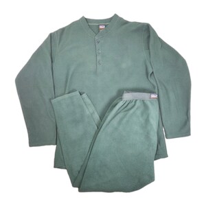 May include: A sage green long-sleeve fleece pajama set consisting of a henley top with three buttons at the neckline and matching elastic-waist pants. Both pieces feature a soft, brushed texture and a small brand label at the collar and waistband.