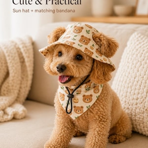 Pode incluir: Um conjunto de chapéu de sol e bandana a condizer para animais de estimação em cor creme, com um padrão repetitivo de caras de urso castanhas, folhas verdes e potes de mel. O chapéu tem uma aba larga e a bandana inclui um cordão preto ajustável.
