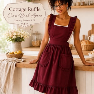 May include: A deep burgundy cross-back apron featuring ruffled shoulder straps, a gathered waist, two front pockets with ruffled edges, and a ruffled hem. The text "Cottage Ruffle Cross-Back Apron Sewing Pattern PDF" is displayed in a decorative frame.