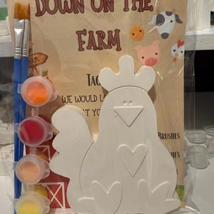 May include: A craft kit in a clear plastic bag featuring a white ceramic chicken figurine, a blue paintbrush, and four small circular paint pots in orange, red, peach, and yellow. The background card displays the text Down on the Farm.