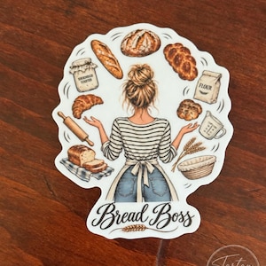 May include: A sticker featuring a person with a messy bun wearing a striped shirt and apron, surrounded by illustrations of bread, a rolling pin, flour, and a sourdough starter jar. The text Bread Boss is printed at the bottom.