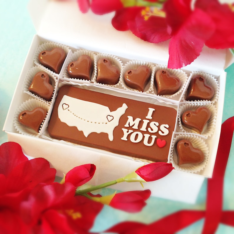 A chocolate box presented in a white box and tied with a bow, with 10 heart chocolates, and one solid bar of chocolate that has phrase "I Love You" 