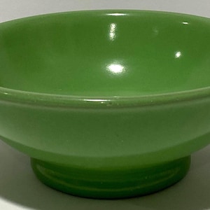 Peut inclure: Un bol vert clair uni avec une finition lisse et brillante et un bord arrondi évasé. Le bol présente une base circulaire sur pied qui surélève le corps principal, créant une silhouette distincte avec un bassin intérieur profond.