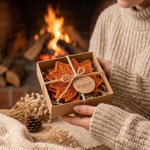 May include: A set of orange crochet leaf-shaped coasters packed in a square cardboard gift box. The coasters are tied with twine and feature a round paper tag with the text Handmade with love printed in black ink on the front of the box.