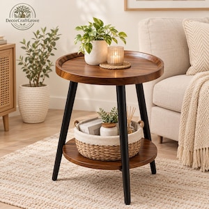 May include: A round side table with a dark wood grain top and bottom shelf, supported by three black metal legs. The top surface holds a potted green plant and a lit candle. A woven basket with a fabric liner sits on the lower shelf.