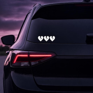 May include: A white vinyl decal featuring three identical heart shapes, each split down the center, applied to the rear window of a dark-colored vehicle. The hearts are arranged horizontally in a row, displaying a clean, solid white graphic design.