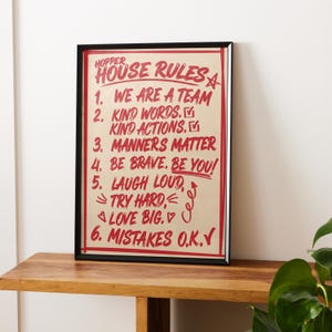 Könnte beinhalten: Ein gerahmter Kunstdruck mit dem Text Hopper House Rules in Rot auf beigem Hintergrund. Die Liste enthält sechs Regeln: We are a team, Kind words and actions, Manners matter, Be brave and you, Laugh loud, try hard, love big und Mistakes O.K.