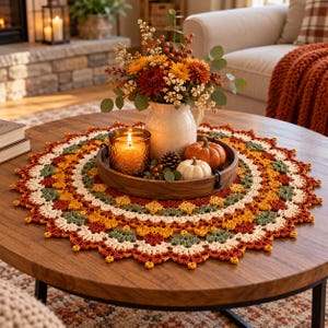 May include: A round, crocheted doily featuring a scalloped edge and a repeating pattern of autumn-colored yarn in shades of burnt orange, deep red, olive green, and cream, arranged in concentric circles to create a decorative table centerpiece.