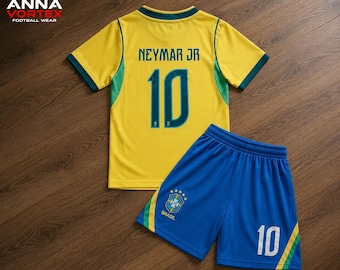 Op de afbeelding: Een geel shirt met korte mouwen en groene accenten, voorzien van de naam NEYMAR JR en het nummer 10 in donkerblauw. Gecombineerd met een blauwe short met een gele en groene zijstreep, het nummer 10 en het embleem van het Braziliaanse elftal.