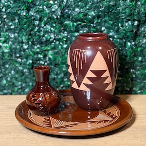 May include: A set of three brown ceramic pieces including a large vase, a small vase, and a round plate. Each piece features a glossy dark brown glaze with contrasting matte tan geometric patterns consisting of triangles and linear etchings.