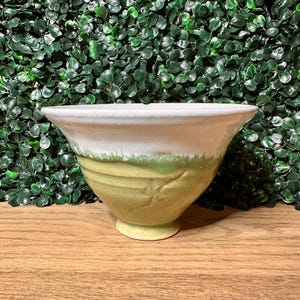 May include: A ceramic bowl featuring a wide, flared rim and a tapered base. The upper portion of the bowl is finished in a smooth white glaze, while the lower section displays a textured, light green glaze with subtle horizontal ridges.