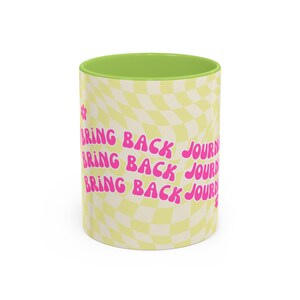 May include: A ceramic mug with a lime green interior and a pale yellow and white wavy checkerboard pattern on the exterior. The text BRING BACK JOURNALS is printed in a repeating pink font across the surface, accompanied by small pink flowers.
