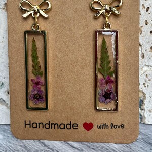 Örhängen med pressade blommor och harts: Lila växter, ormbunksblad. Rektangulär bezel. (Guldfärgade rosettstolpar)