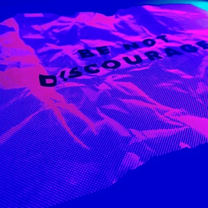 May include: A crumpled piece of paper with the words "Be Not Discouraged" printed in black on a pink and blue background.