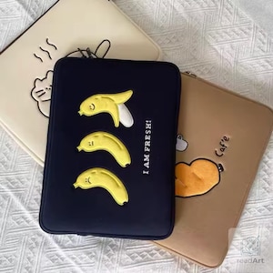 May include: Three rectangular laptop sleeves in black, cream, and tan. The black sleeve features three yellow banana graphics and the text I AM FRESH!. The cream sleeve has a cat outline, and the tan sleeve shows a bread graphic with the text Caf'e.