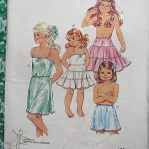 May include: Vintage sewing pattern featuring illustrations of young girls in various sleepwear designs. The drawings include a light green slip, a white tiered dress, a pink petticoat, and blue shorts. The pattern is designed by Kerstin Martensson.