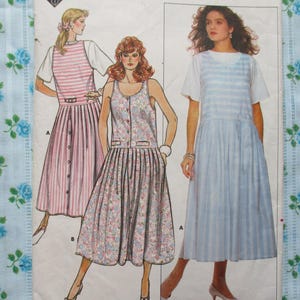 May include: A vintage sewing pattern featuring illustrations of three different dresses. The dresses include a pink and white striped dress, a floral print dress, and a blue and white striped dress. The background is a light blue floral fabric.