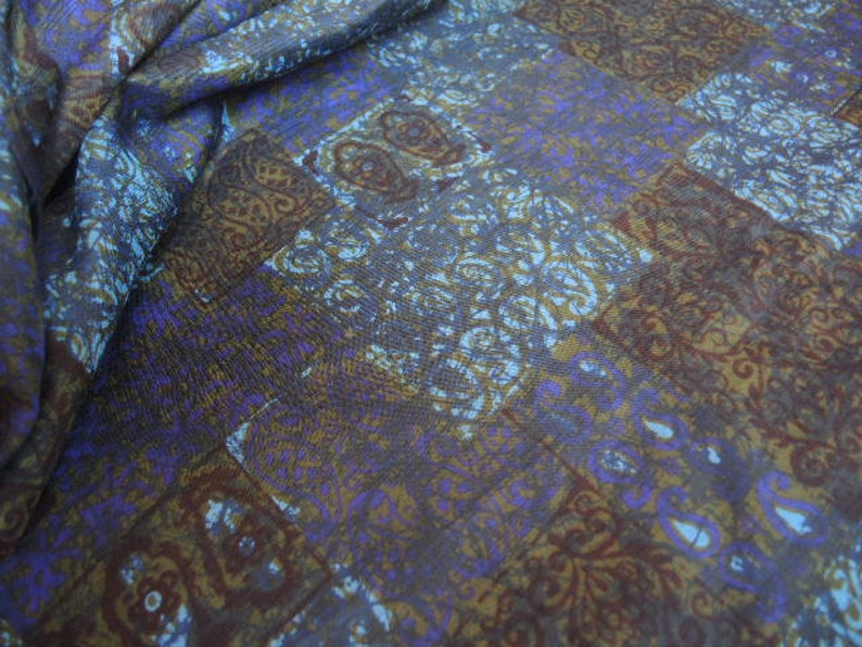 May include: A fabric with a blue, brown, and white patterned design. The pattern is a repeating geometric design with a paisley-like motif.