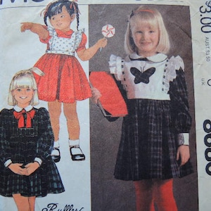 May include: A sewing pattern for a child's dress. The pattern includes two different styles, one with a plaid skirt and a white bodice with a butterfly design, and the other with a red skirt and a white bodice with a bib. The pattern number is 8680.