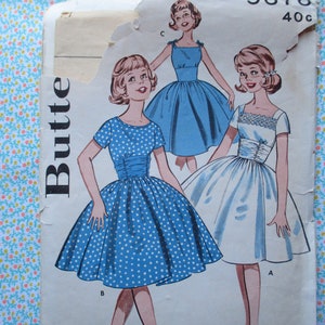 Puede incluir: Patrón de costura vintage para un vestido con tres estilos diferentes. El patrón es para un vestido con un corpiño ajustado y una falda completa. El vestido se muestra en tres colores diferentes: azul con lunares blancos, azul sólido y blanco. El patrón está etiquetado como "Butte 40c".
