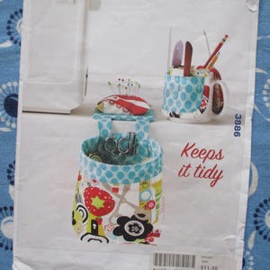 May include: A sewing organiser set with a pin cushion, a container with scissors, and a mug holding pencils and tools. The set features a blue and white polka dot pattern and a floral design. The text "Keeps it tidy" is also visible.