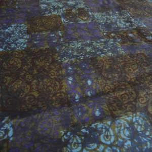 May include: A close-up of a fabric with a repeating pattern of brown, blue, and purple swirls. The fabric has a soft, textured feel.