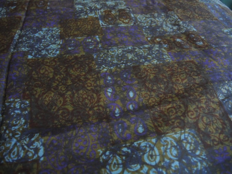 May include: A close-up of a fabric with a repeating pattern of brown, blue, and purple swirls. The fabric has a soft, textured feel.
