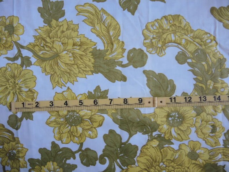 May include: White fabric with a repeating pattern of yellow flowers and green leaves. A ruler is placed across the fabric, showing measurements in inches.