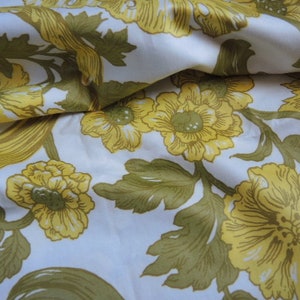 May include: White fabric with a floral pattern featuring yellow flowers and green leaves. The fabric has a silky texture.