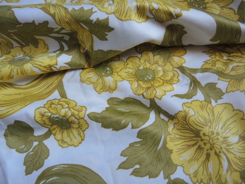 May include: White fabric with a floral pattern featuring yellow flowers and green leaves. The fabric has a silky texture.