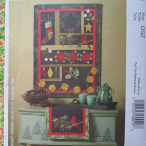 May include: A quilting pattern for a Christmas-themed wall hanging and table runner. The pattern features a red, green, and brown color scheme with images of pine cones, cardinals, and a stocking. The pattern is titled "Wallies wallpaper cutouts 12137 Moose and Trees".