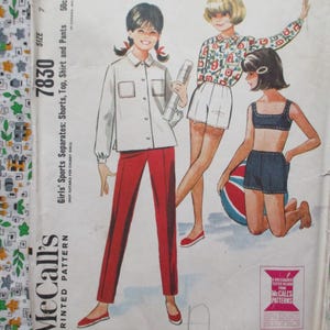 Könnte beinhalten: Vintage McCall's Schnittmuster 7830 für Mädchen-Sport-Separates. Die Illustration zeigt ein Mädchen in einem weißen Hemd und einer roten Hose sowie zwei weitere Mädchen in Shorts und Oberteilen. Das Muster umfasst Shorts, Oberteil, Hemd und Hose.