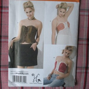 May include: A sewing pattern featuring three different styles of tops. The first top is a brown corset with a black skirt. The second top is a red and white floral top with a white skirt. The third top is a red and white floral corset with blue jeans. The pattern is from Simplicity.com.