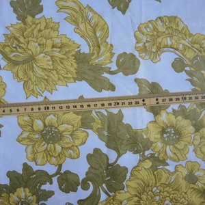 May include: White fabric with a repeating pattern of yellow flowers and green leaves. The fabric is measured with a ruler, showing the scale of the pattern.