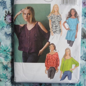 May include: A sewing pattern showcasing five distinct top styles, all featuring cold shoulder detailing. The tops are displayed in a range of colours and patterns, including a burgundy top, a black and white patterned top, a red and white patterned top, a blue and white striped top, and a green top.