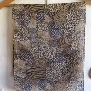 May include: A rectangular scarf with a mixed animal print design, including leopard spots and zebra stripes, in shades of brown and tan. The scarf is hanging on a wooden hanger.