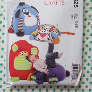 May include: A sewing pattern featuring designs for children's bean bag chairs shaped like cartoon animals. The pattern includes a blue dog, a zebra, a red bear, and a purple bear. The pattern is labelled with the word "CRAFTS".