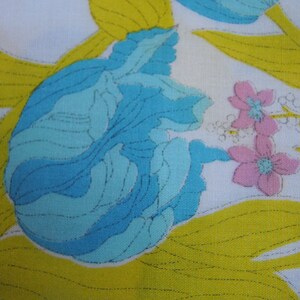 May include: A white fabric with a blue and yellow floral pattern. The flowers are stylized and have a retro look. The fabric has a quilted texture.