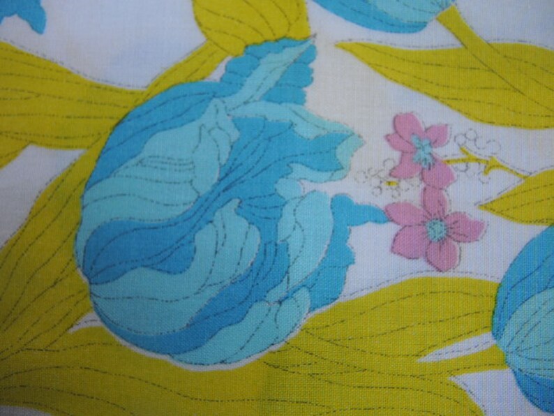 May include: A white fabric with a blue and yellow floral pattern. The flowers are stylized and have a retro look. The fabric has a quilted texture.