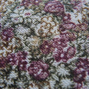May include: Close-up of a fabric with a floral pattern. The fabric is white with brown, pink, and purple flowers.