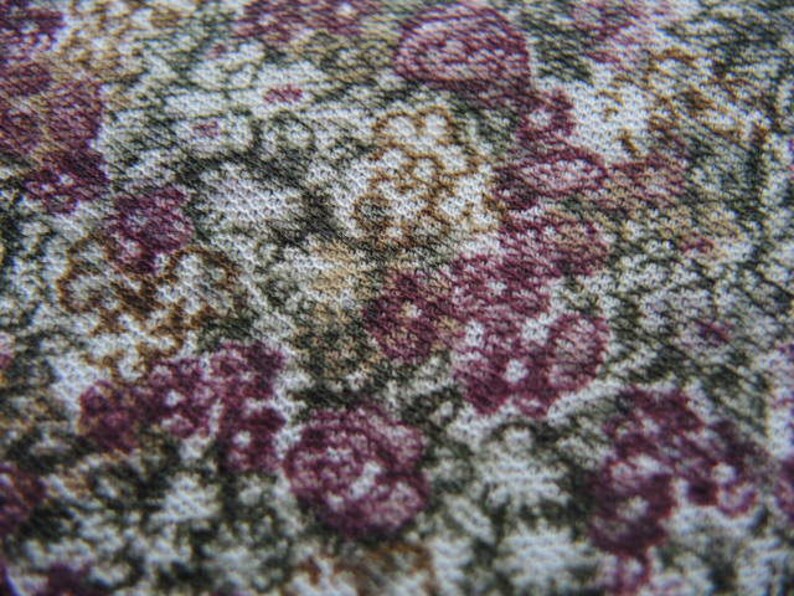 May include: Close-up of a fabric with a floral pattern. The fabric is white with brown, pink, and purple flowers.