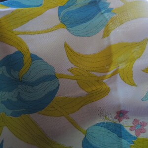 May include: A white fabric with a blue and yellow floral pattern. The flowers are stylized and resemble tulips. The fabric has a smooth, silky texture.