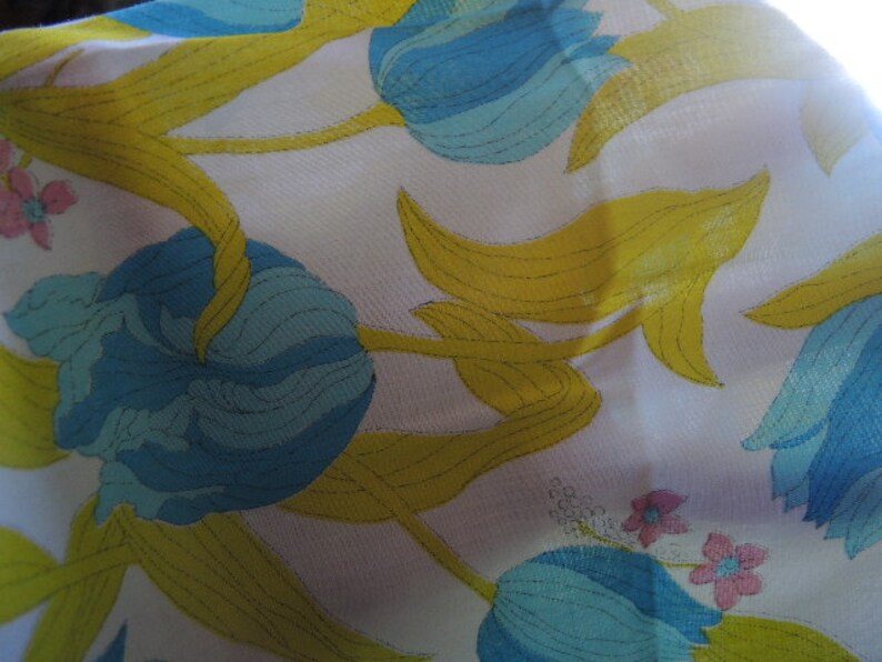 May include: A white fabric with a blue and yellow floral pattern. The flowers are stylized and resemble tulips. The fabric has a smooth, silky texture.